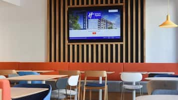 Un intérieur de restaurant moderne, avec un téléviseur fixé au mur, des tables et des chaises disposées de manière agréable, et un plafond en bois au design original.
