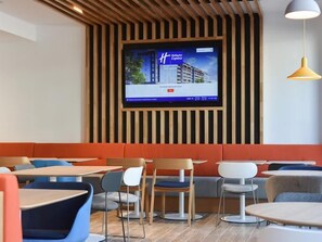 Un intérieur de restaurant moderne, avec un téléviseur fixé au mur, des tables et des chaises disposées de manière agréable, et un plafond en bois au design original.