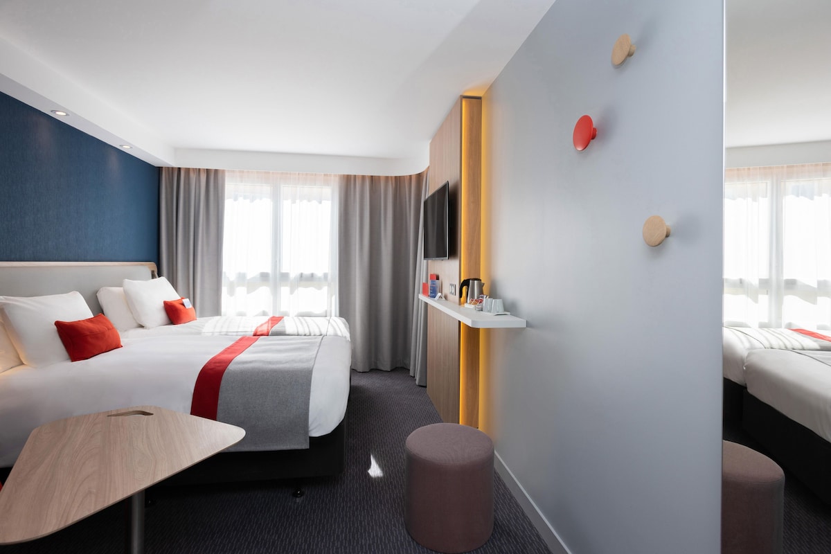 Una habitación de hotel moderna con una cama, una mesita de noche y un televisor montado en la pared.