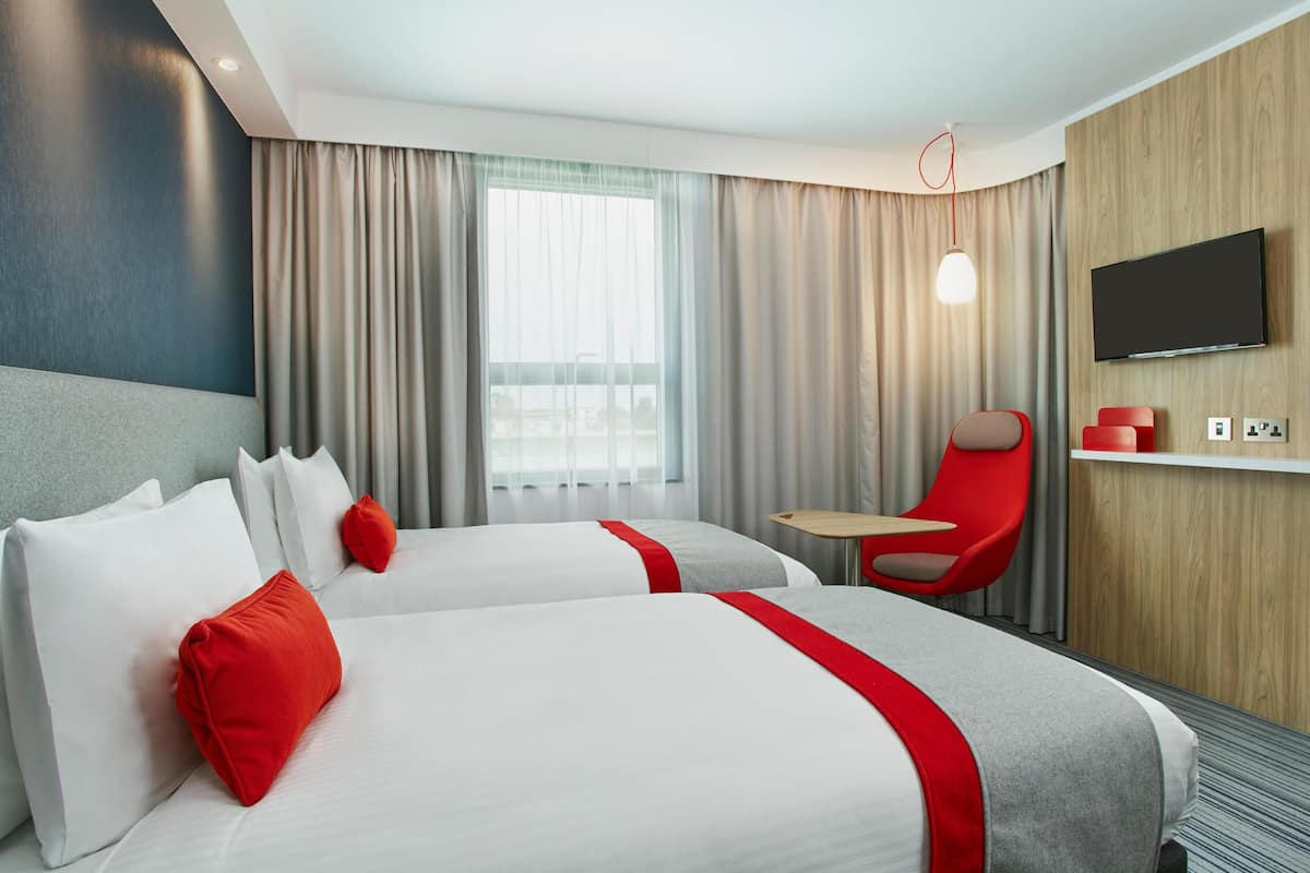 A hotel room with two beds, a TV, a red chair, and a small table.