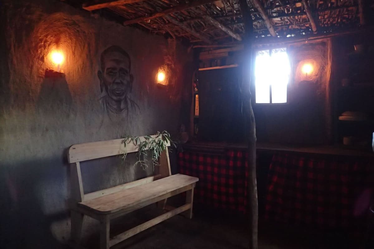 A dimly lit room with a wooden bench, a wall-mounted plant, and a window with a red checkered curtain.