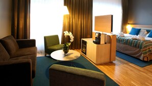 Habitación de hotel con cama, escritorio, silla, sofá y una mesita con un florero.