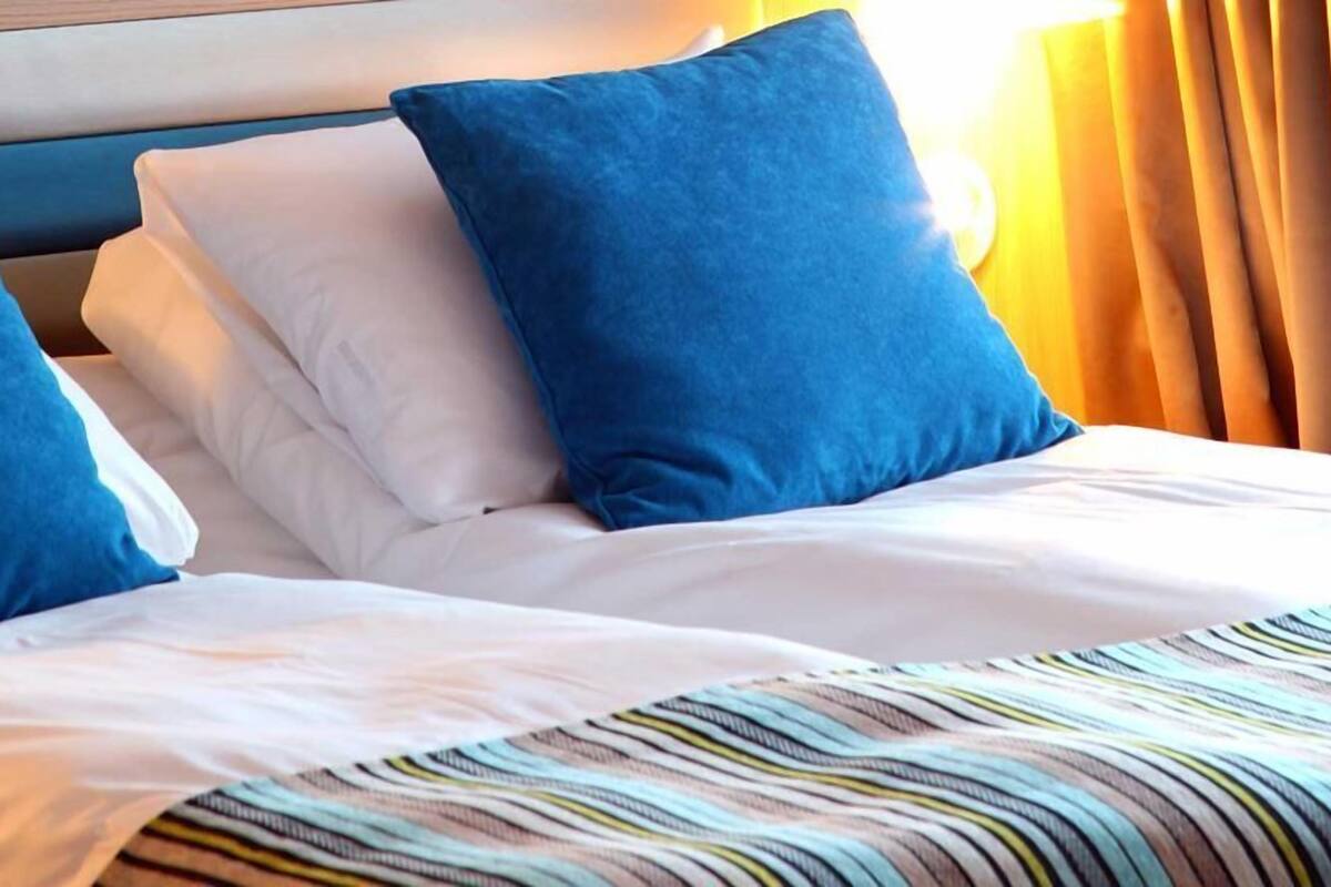 Hotelkamer met een bed, voorzien van wit- en blauw beddengoed, een gestreept plaid en een hoofdbord met een houten afwerking.