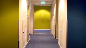 A hotel corridor with a carpeted floor, doors on both sides, and a green exit sign above the door. - Thon Hotel Bronnoysund (Brønnøy)