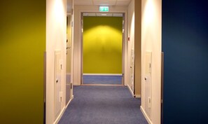 Pasillo de hotel con piso alfombrado, puertas a ambos lados y una señal de salida verde sobre la puerta.