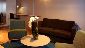 Una sala de estar moderna con un sofá marrón, un sillón verde, una mesa redonda blanca y una orquídea en maceta.