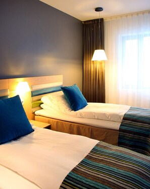 Habitación de hotel con dos camas, cabecero, lámpara de noche, ventana con cortinas y lámpara colgante.