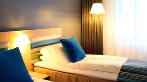 Habitación de hotel con dos camas, cabecero, lámpara de noche, ventana con cortinas y lámpara colgante.