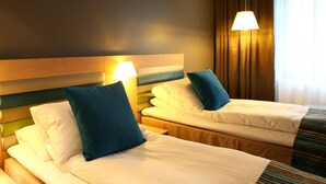 Habitación de hotel con dos camas, cada una con un cojín y una lámpara de noche.