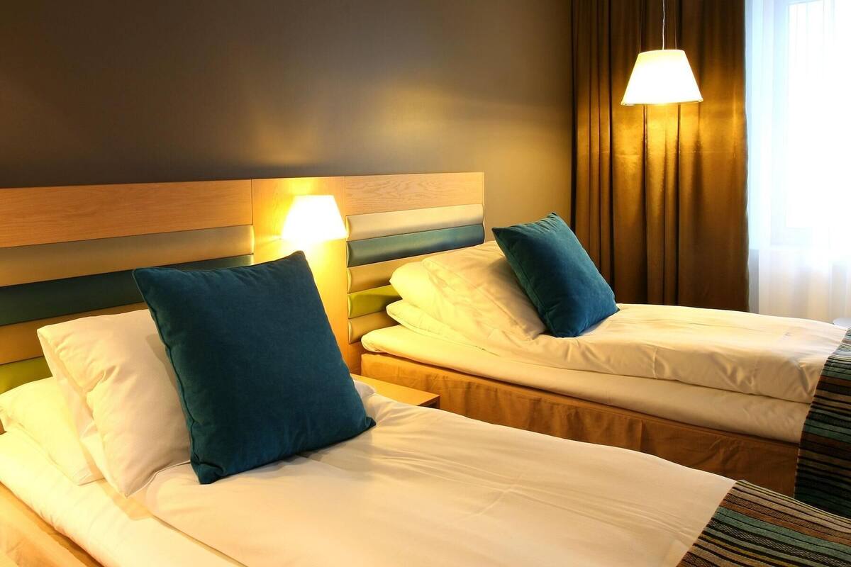 Een hotelkamer met twee bedden, elk voorzien van een kussen en een bedlampje.