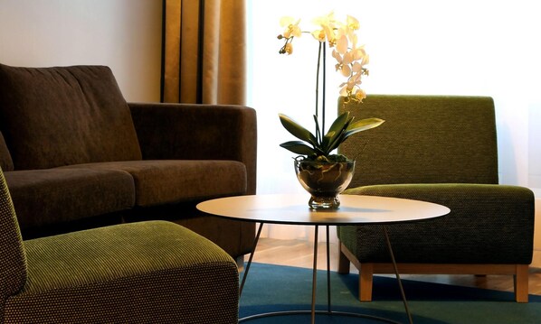 A room with a brown sofa, a green armchair, a round table with a plant, and a window with curtains. - Thon Hotel Bronnoysund (Brønnøy)