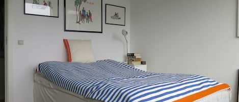 Un dormitorio con una cama, una mesita de noche, una lámpara y tres cuadros en la pared.