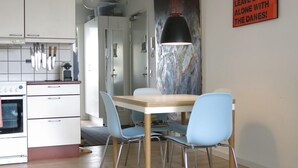 Una cocina moderna con armarios blancos, una estufa y cuchillos colgando. Hay una mesa de comedor con sillas azules y una lámpara colgante.