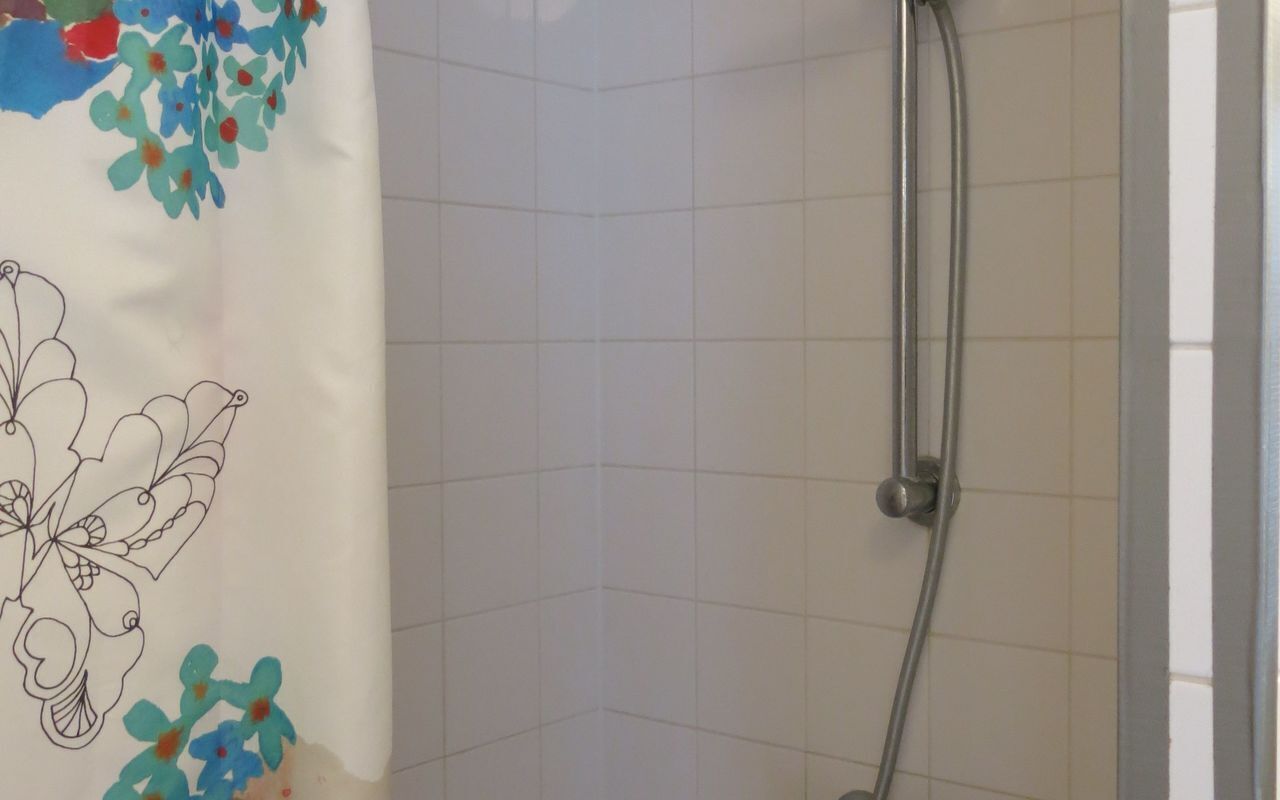 A shower area with a white tiled wall, a showerhead, and a colorful shower curtain with floral designs.
