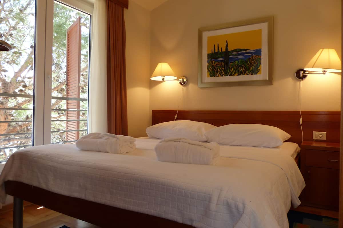 A hotel room with a bed, two wall-mounted lamps, a painting, and a window with curtains.