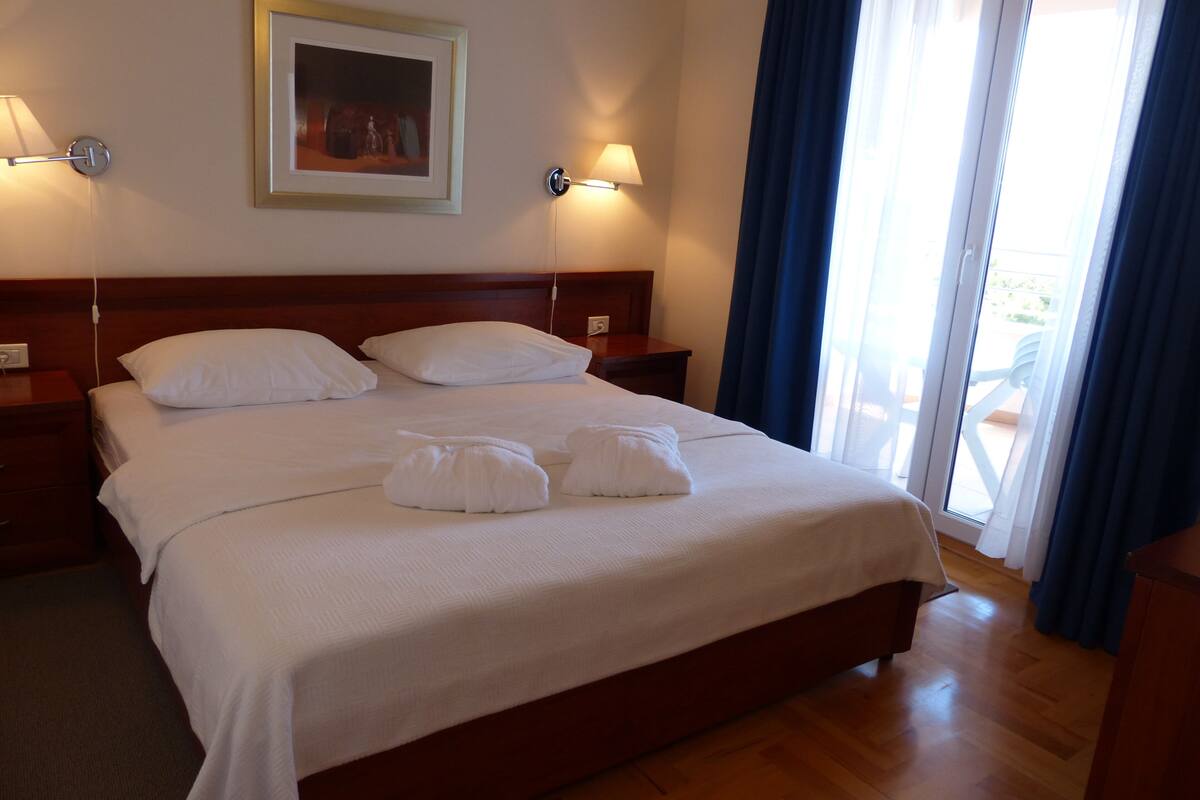 A neatly made bed with white linens and pillows, a wooden headboard, bedside lamps, and a framed picture on the wall.
