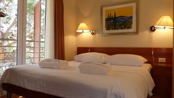 A hotel room with a bed, two wall-mounted lamps, a painting, and a window with curtains.