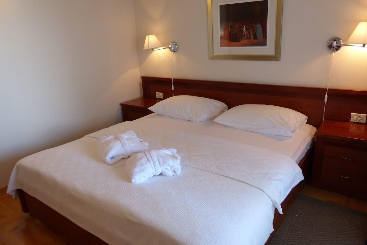 A neatly made bed with white linens and towels, a wooden headboard, and bedside lamps.