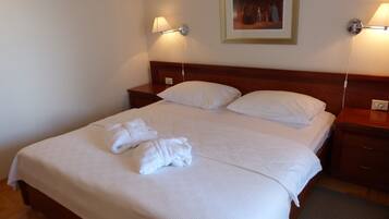 A neatly made bed with white linens and towels, a wooden headboard, and bedside lamps.