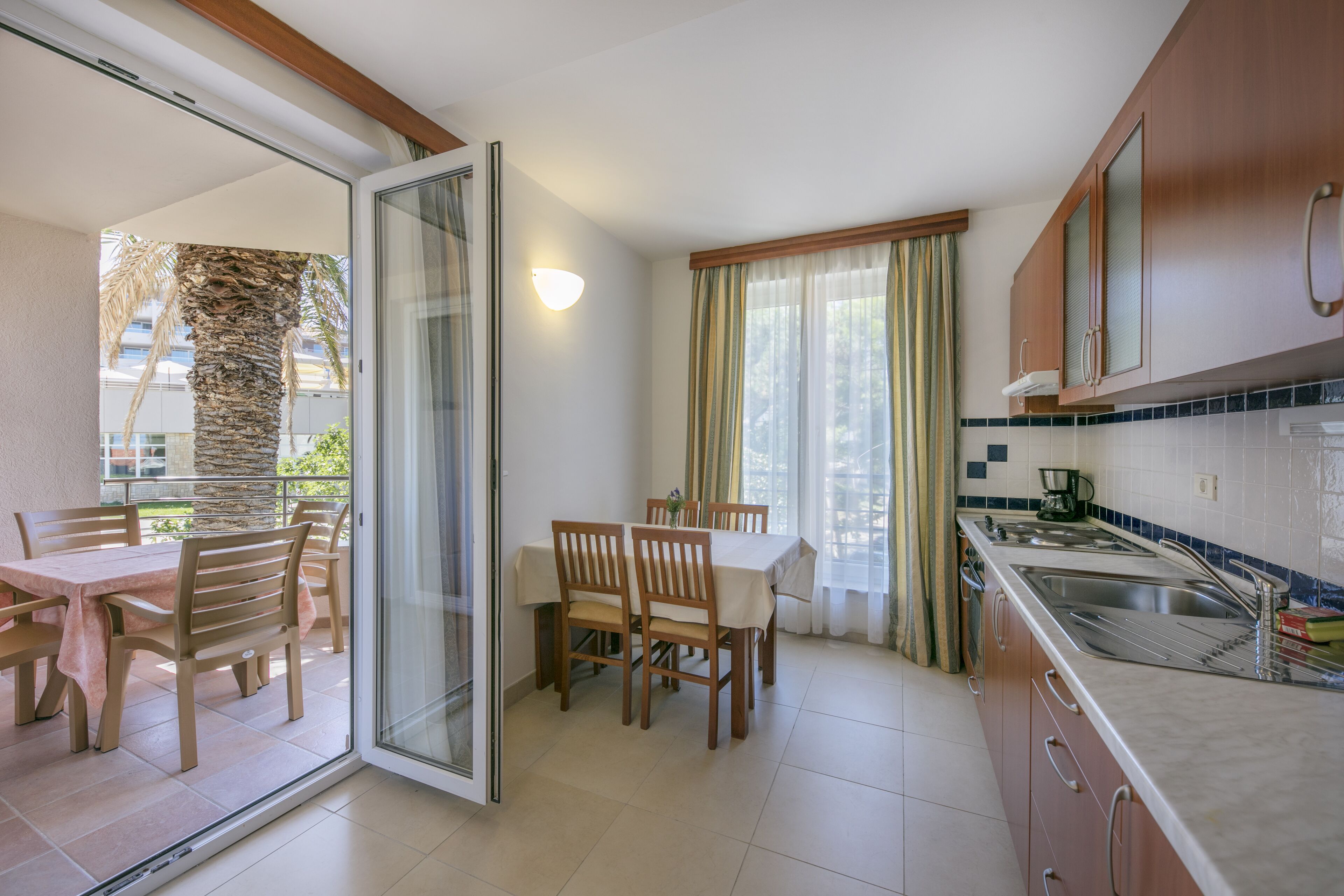 Une cuisine avec un coin repas, une porte-fenêtre coulissante donnant sur un balcon et une vue sur des palmiers.