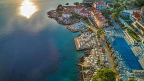 An aerial view of a coastal hotel with a marina, beach umbrellas, and a swimming pool. - Apartments Punta (Mali Losinj)