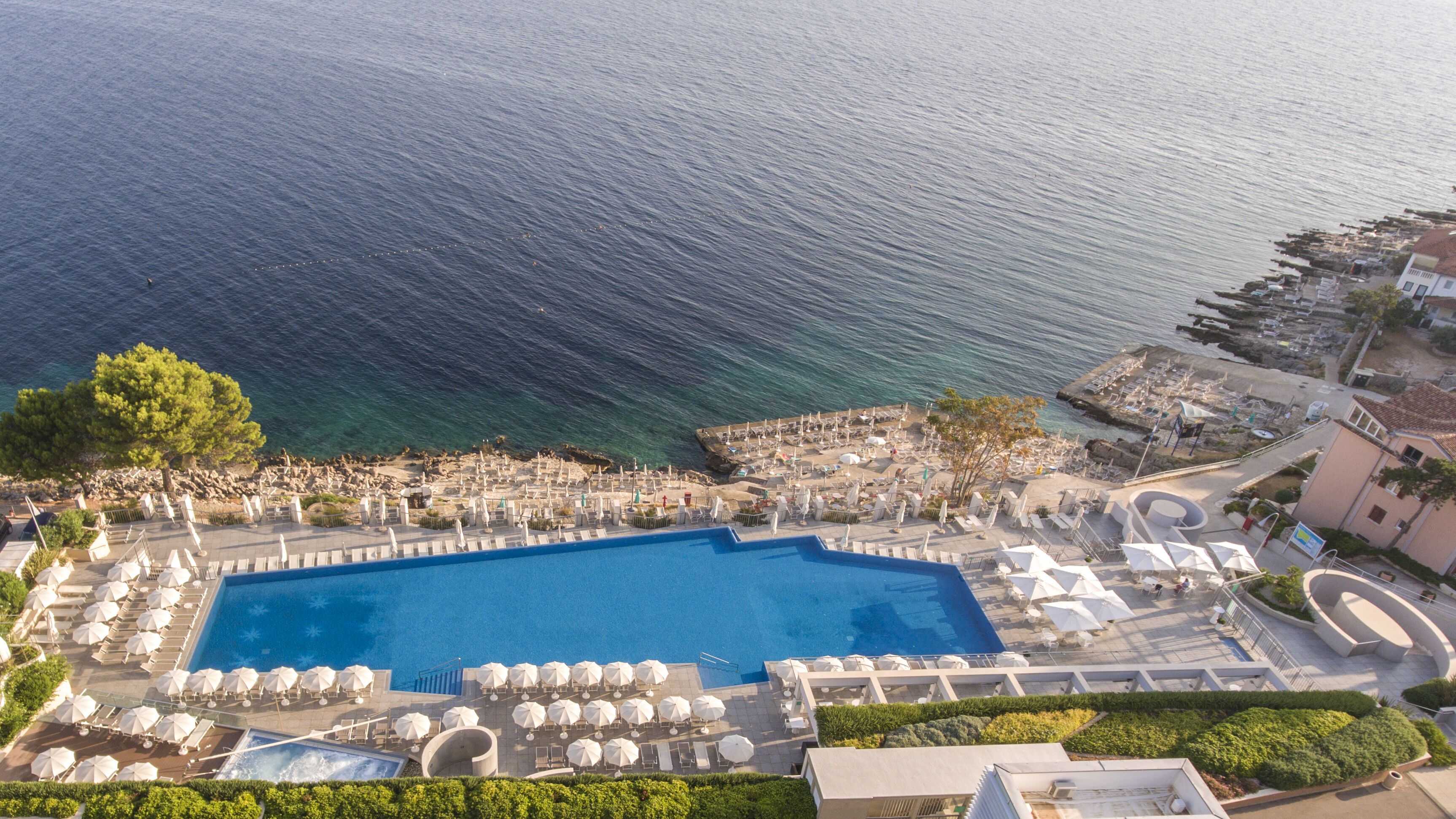 Un resort con una piscina grande, tumbonas y vistas al mar.