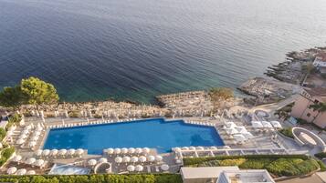 Un resort con una piscina grande, tumbonas y vistas al mar.