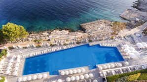 An aerial view of a resort with a large swimming pool, sun loungers, and a rocky coastline. - Apartments Punta (Mali Losinj)