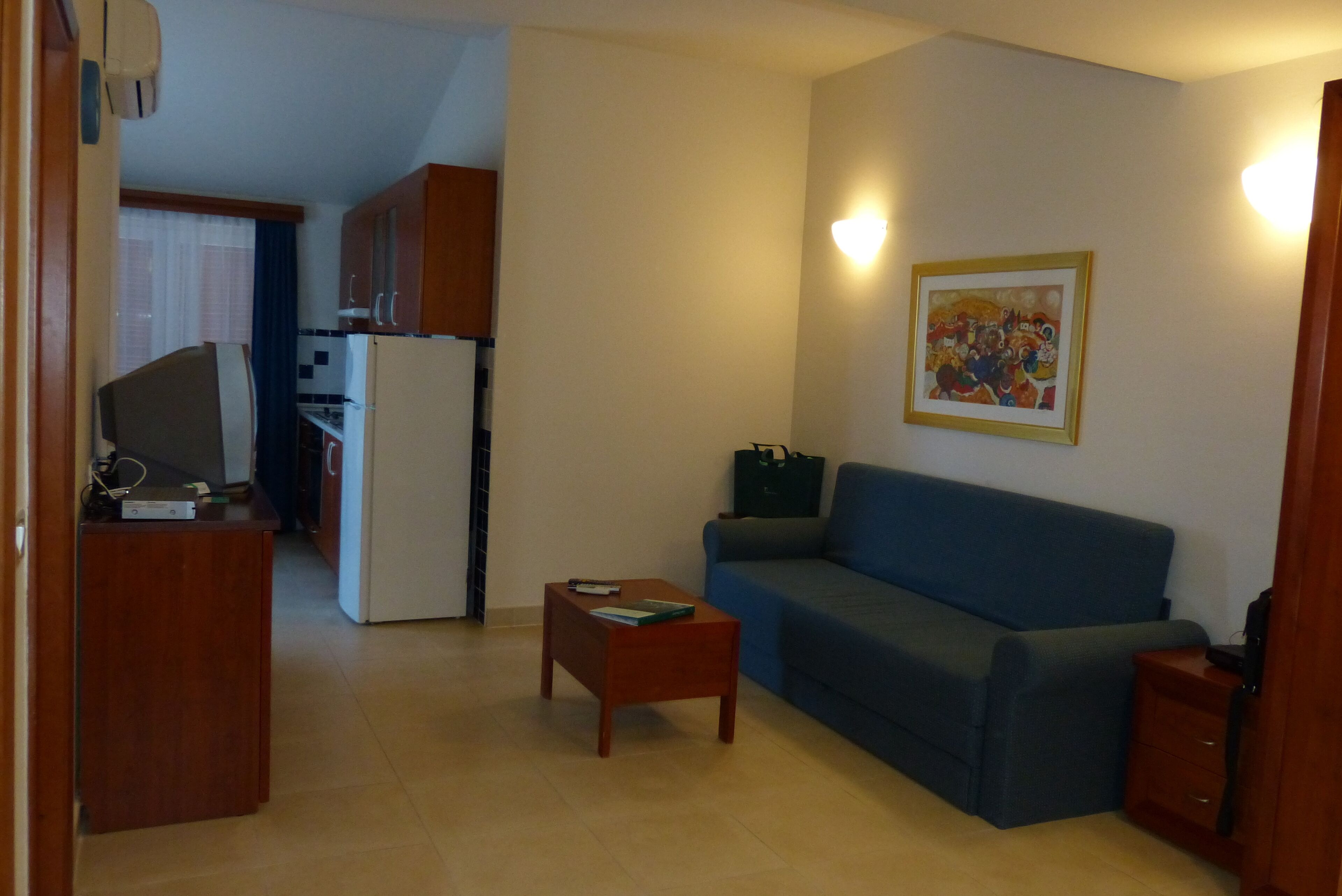 Un espacio habitable pequeño con kitchenette, un sofá, una mesa de centro y un cuadro en la pared.