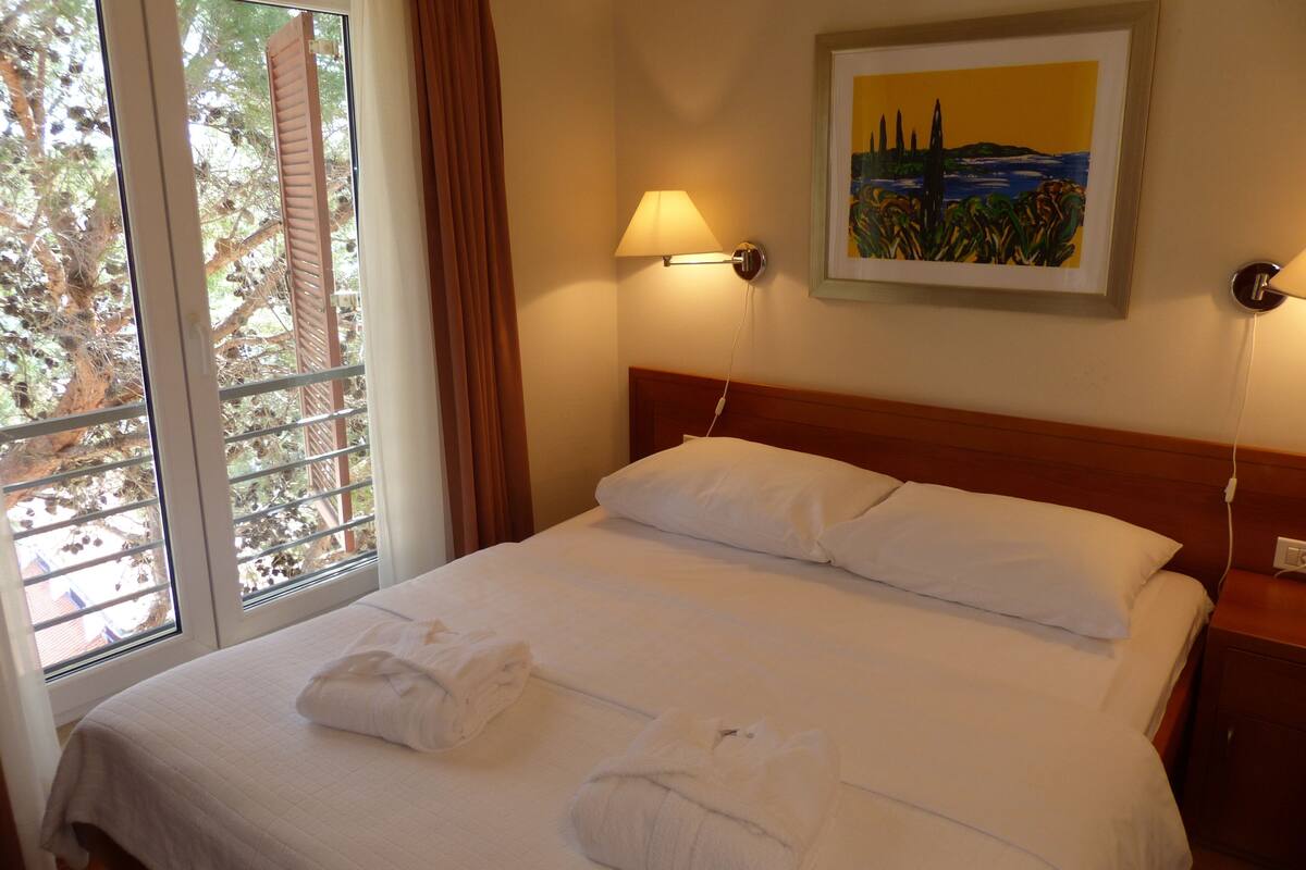 A hotel room with a bed, a painting on the wall, and a window with curtains.