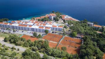 An aerial view of a coastal hotel with multiple buildings, tennis courts, and a parking area.