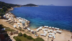 A coastal beach with numerous umbrellas and sun loungers, a clear view of the sea, and a rocky shoreline. - Apartments Punta (Mali Losinj)