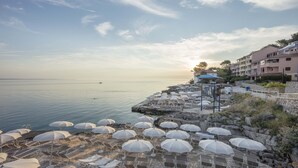 A coastal hotel with a stone terrace, white umbrellas, and lounge chairs. - Apartments Punta (Mali Losinj)