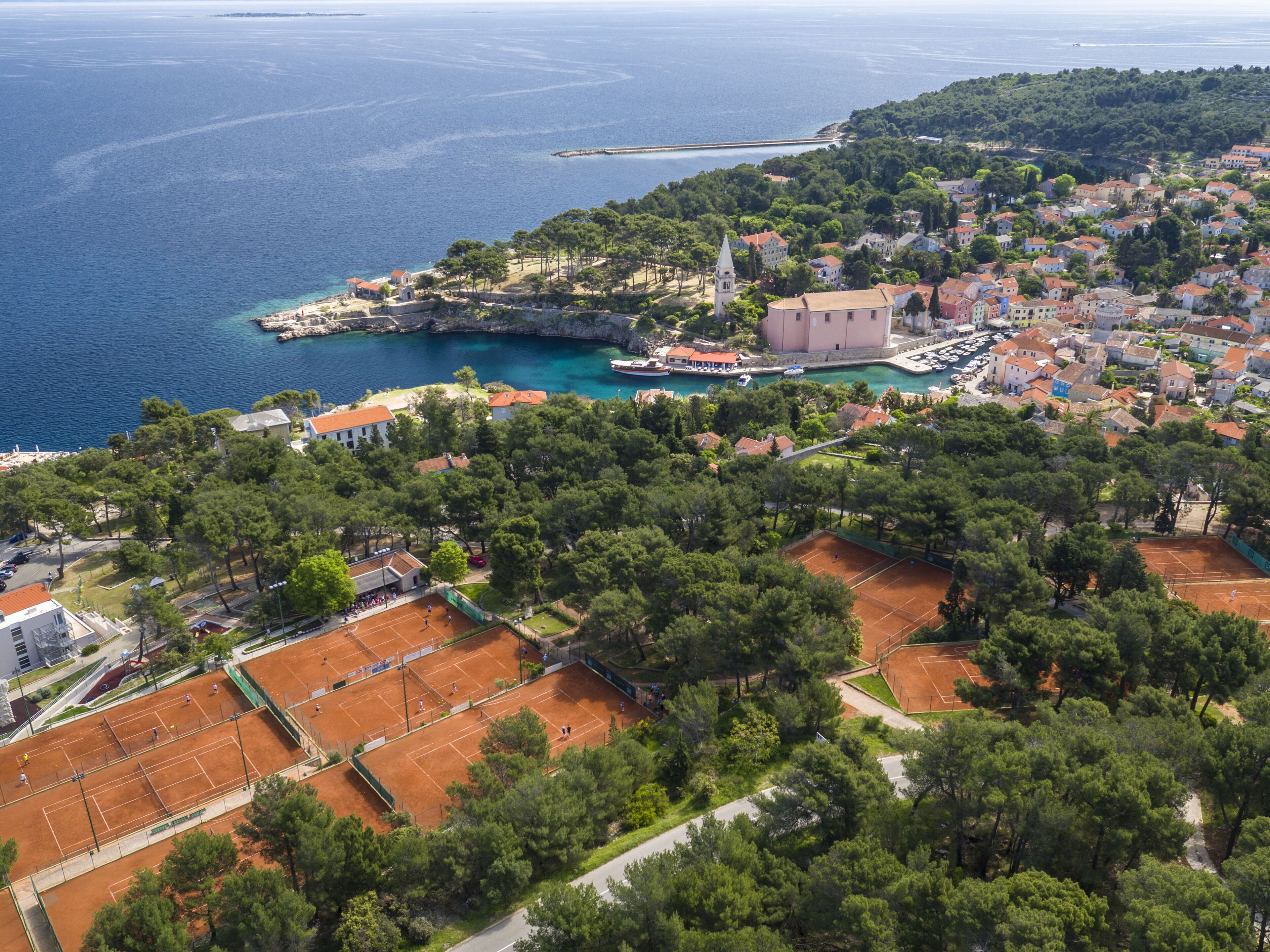 An aerial view of a coastal town with a prominent church, tennis courts, and a marina.