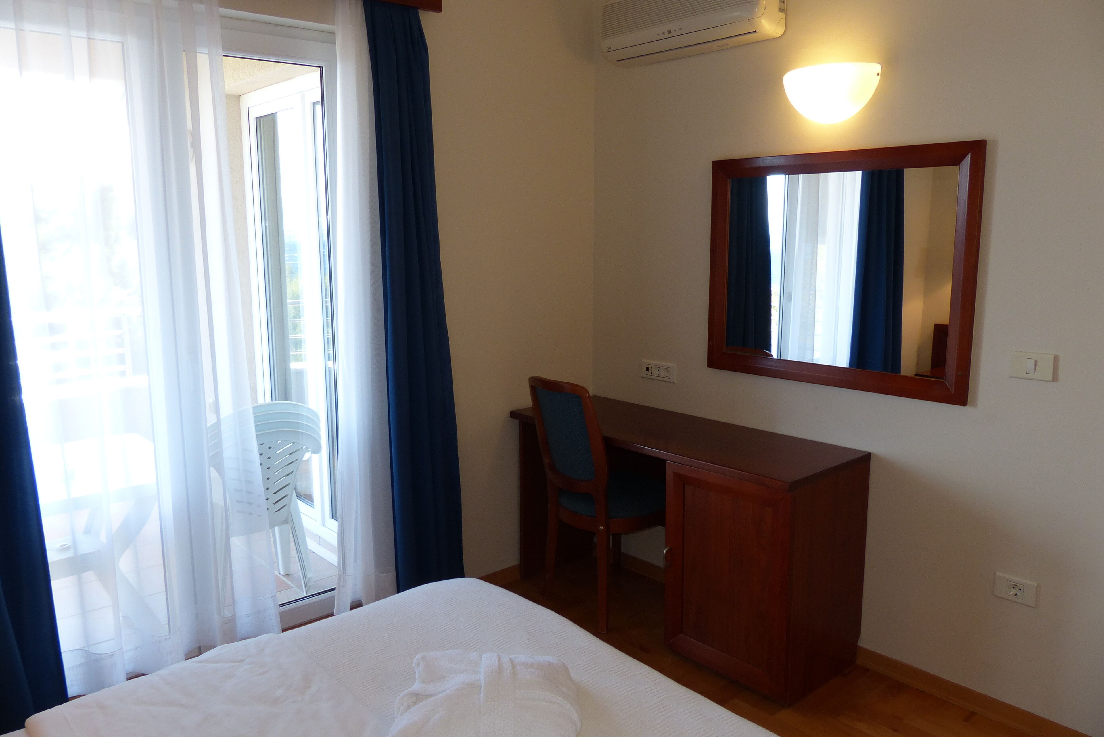 A hotel room with a bed, a desk, a chair, a mirror, and a window with curtains.