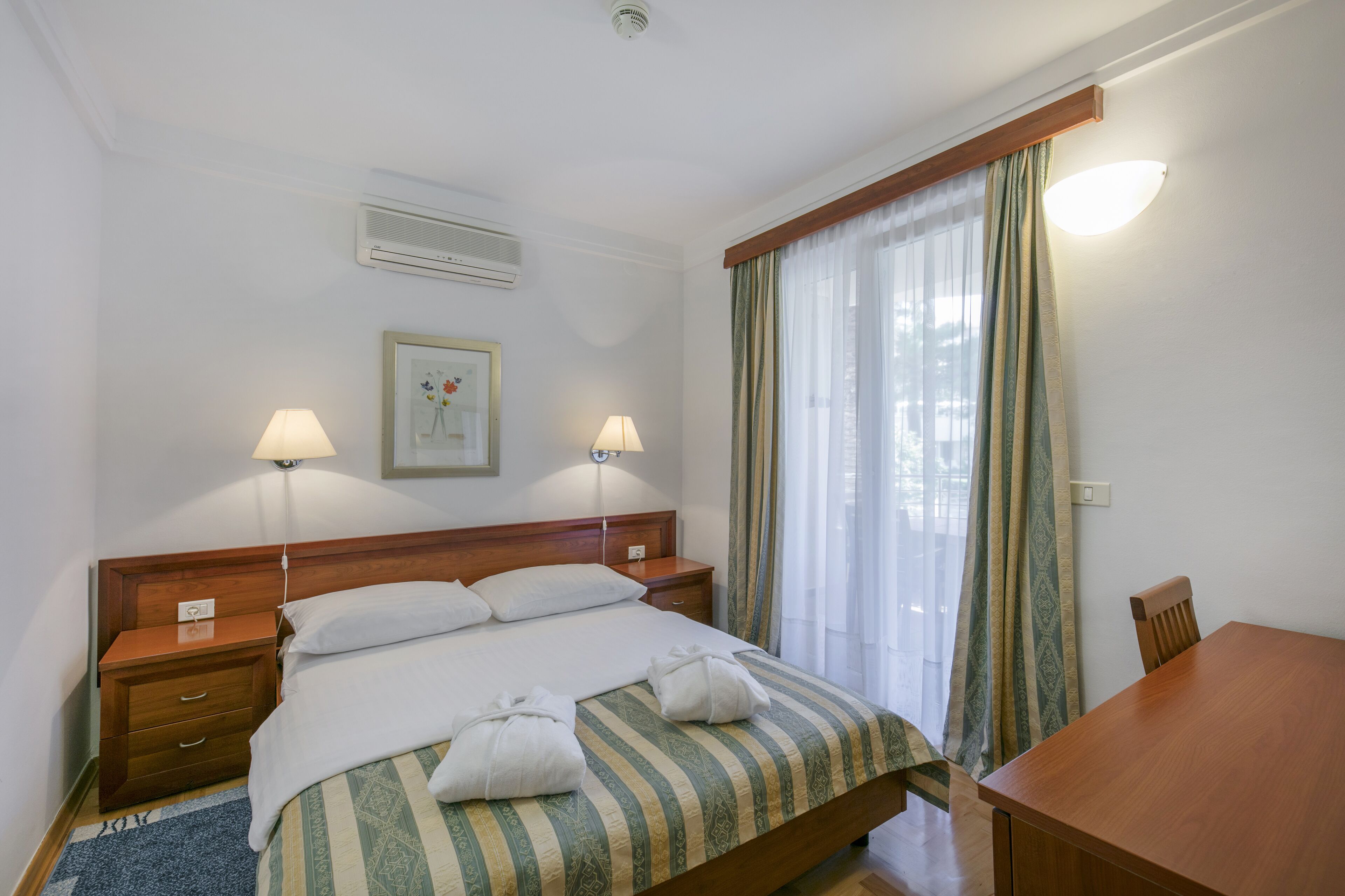 A hotel room with a bed, two bedside tables, a desk, and a chair.