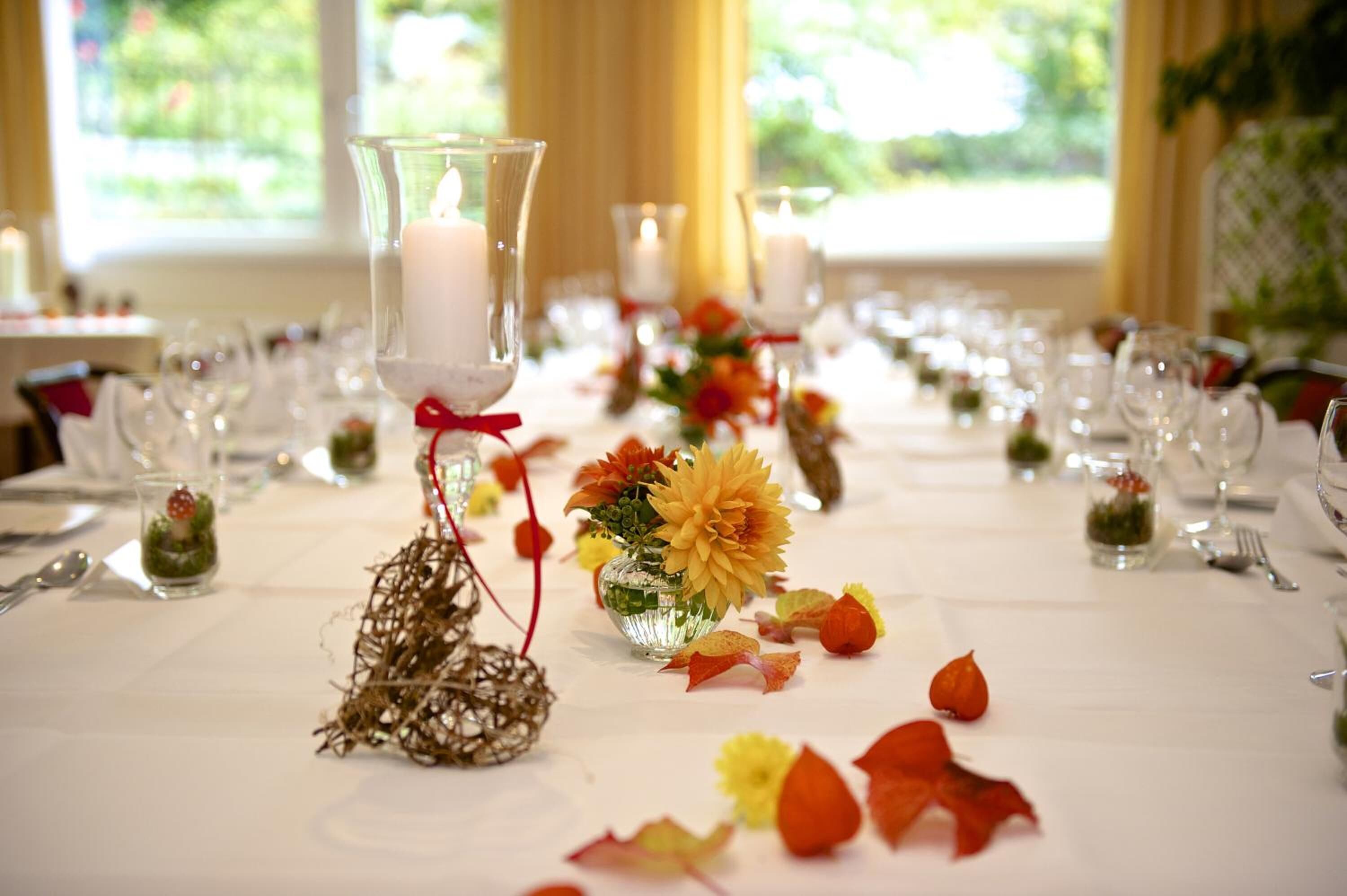 A banquet table set with candles, glass vases with flowers, and scattered petals.
