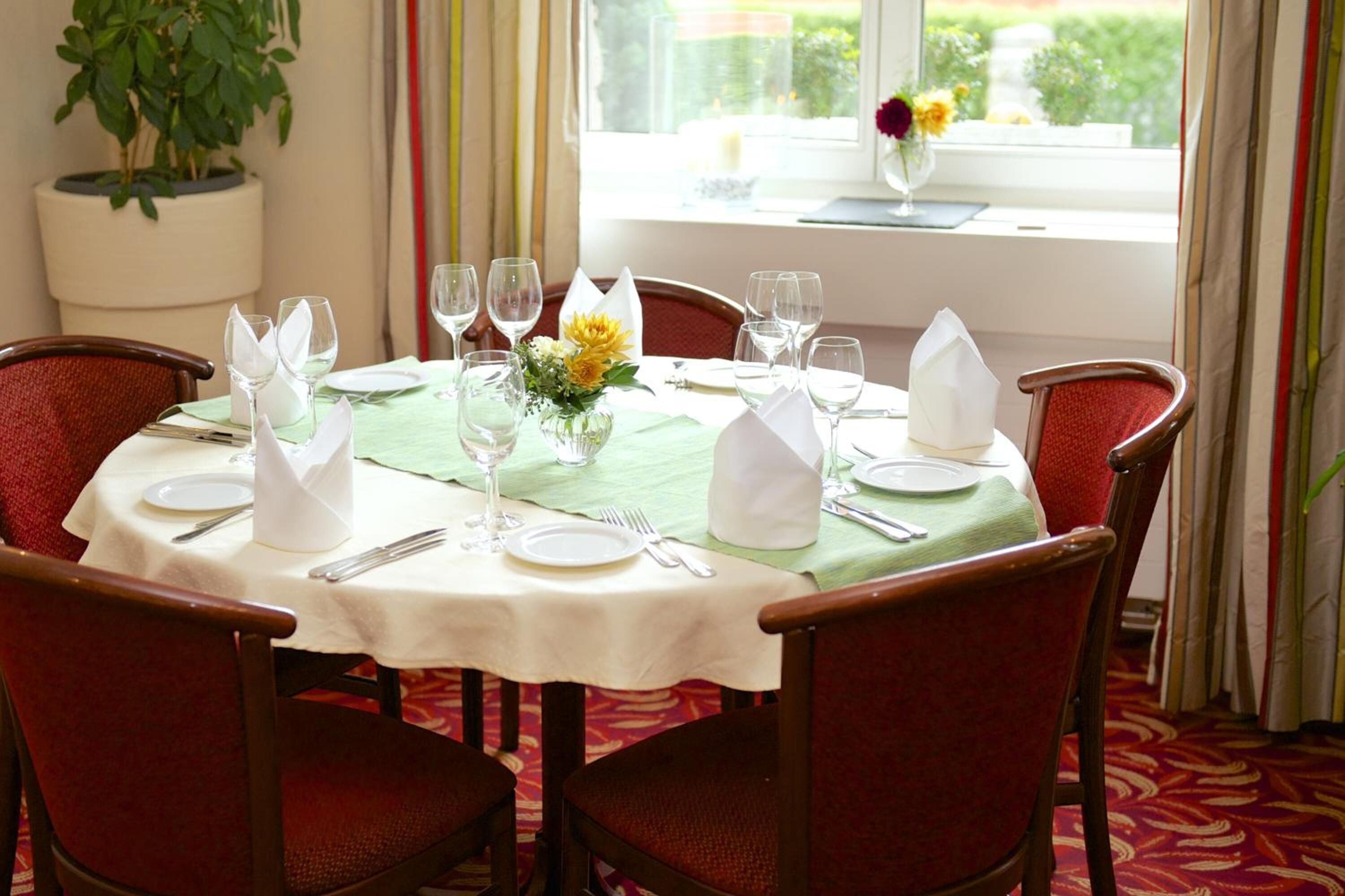A dining table set for four with white tablecloths, green napkins, and a vase with yellow flowers.