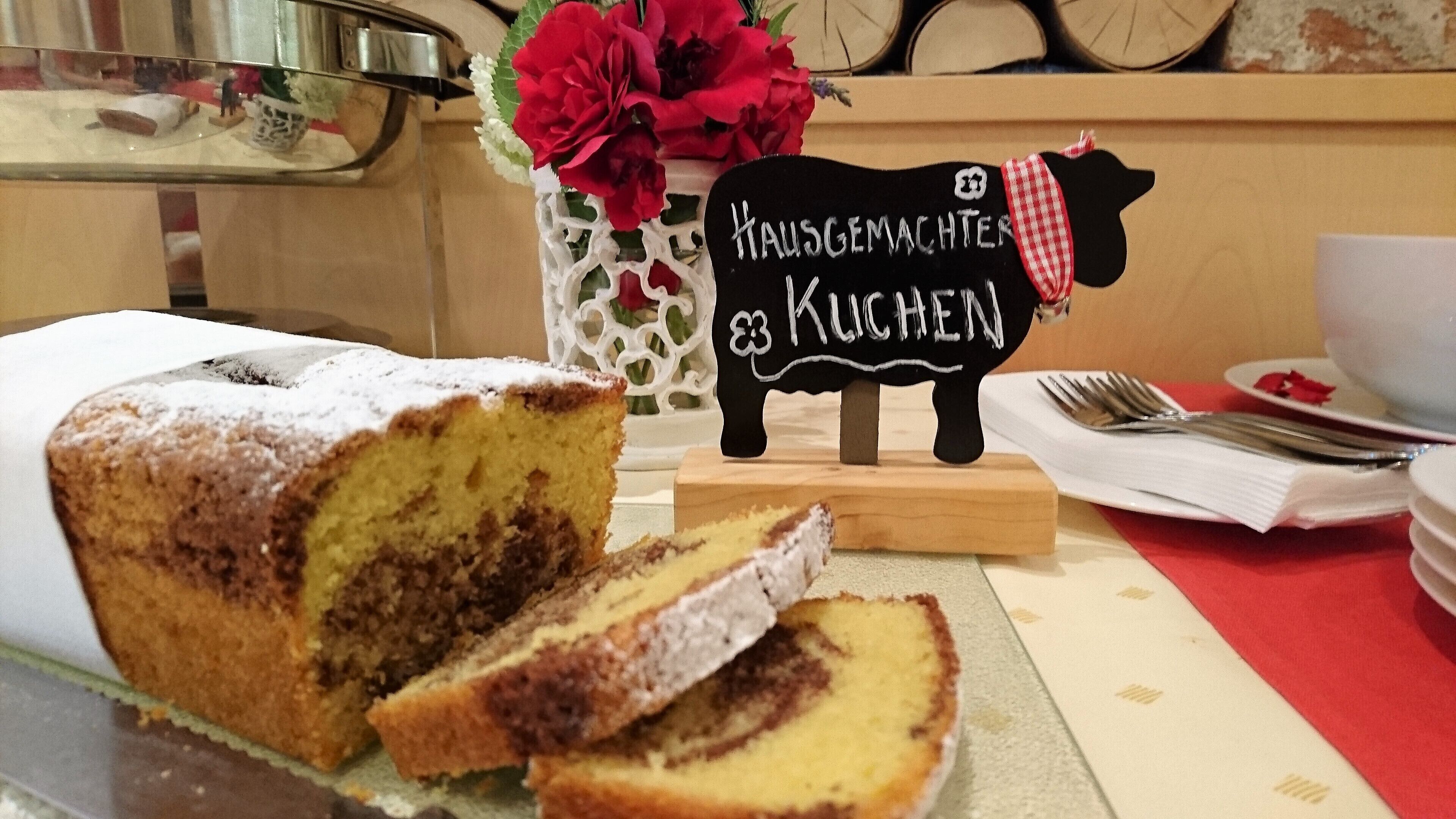 A slice of cake on a plate with a sign that reads "Hausgemachter Kuchen" in the background.