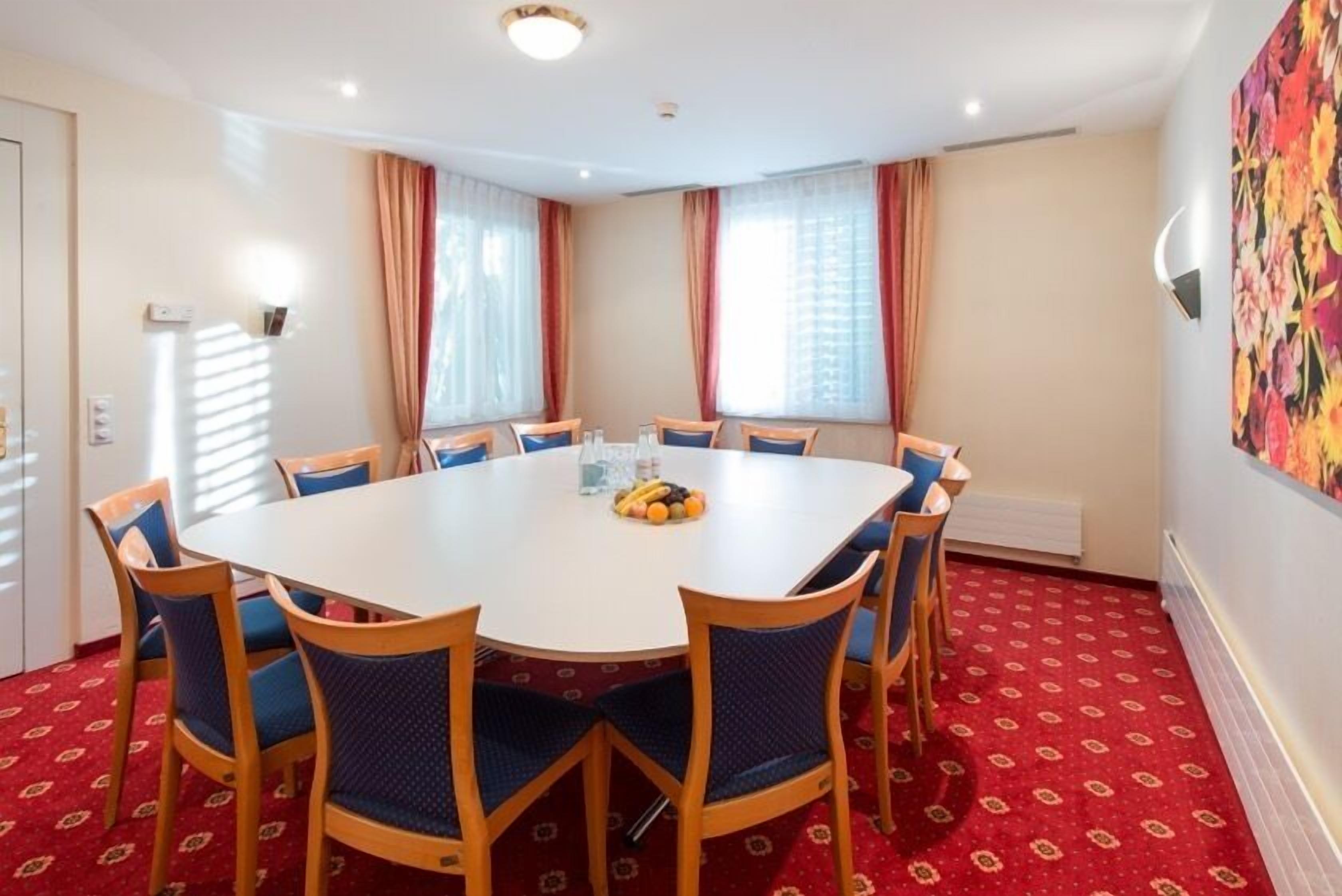 A conference room with a round table, eight chairs, and a fruit bowl on the table.