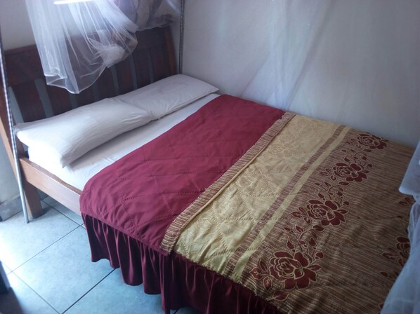 A single bed with a white mattress and two pillows, a red and beige bedspread, and a mosquito net above. - Jalu Guest House (Mwingi)