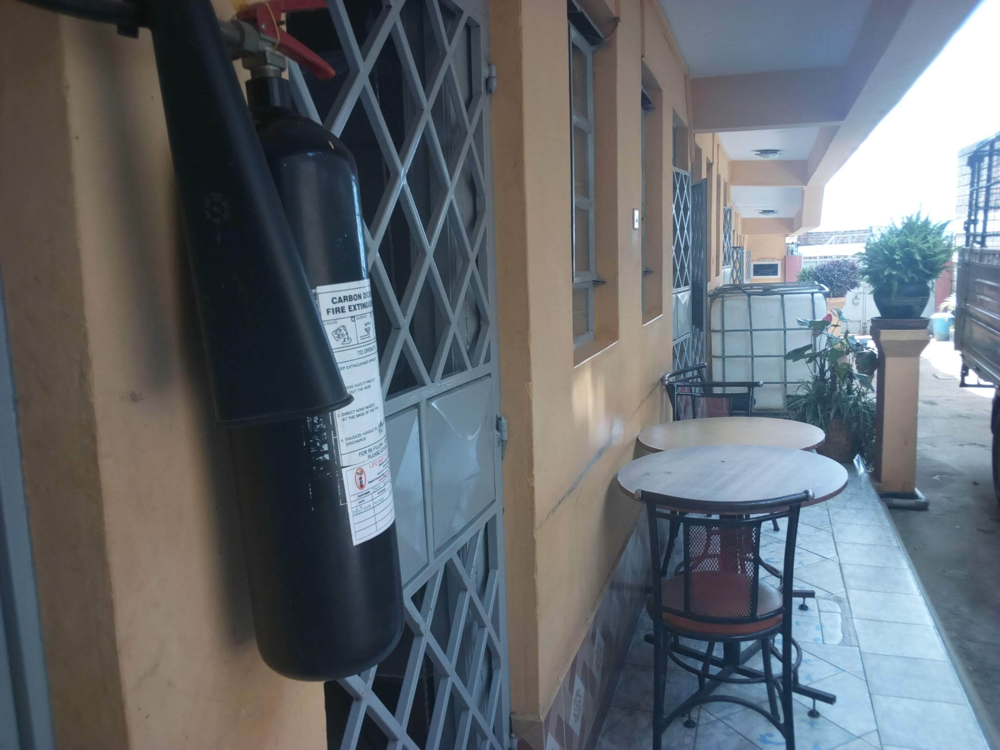 A small outdoor seating area with a table and chairs, a fire extinguisher mounted on the wall, and a metal gate.
