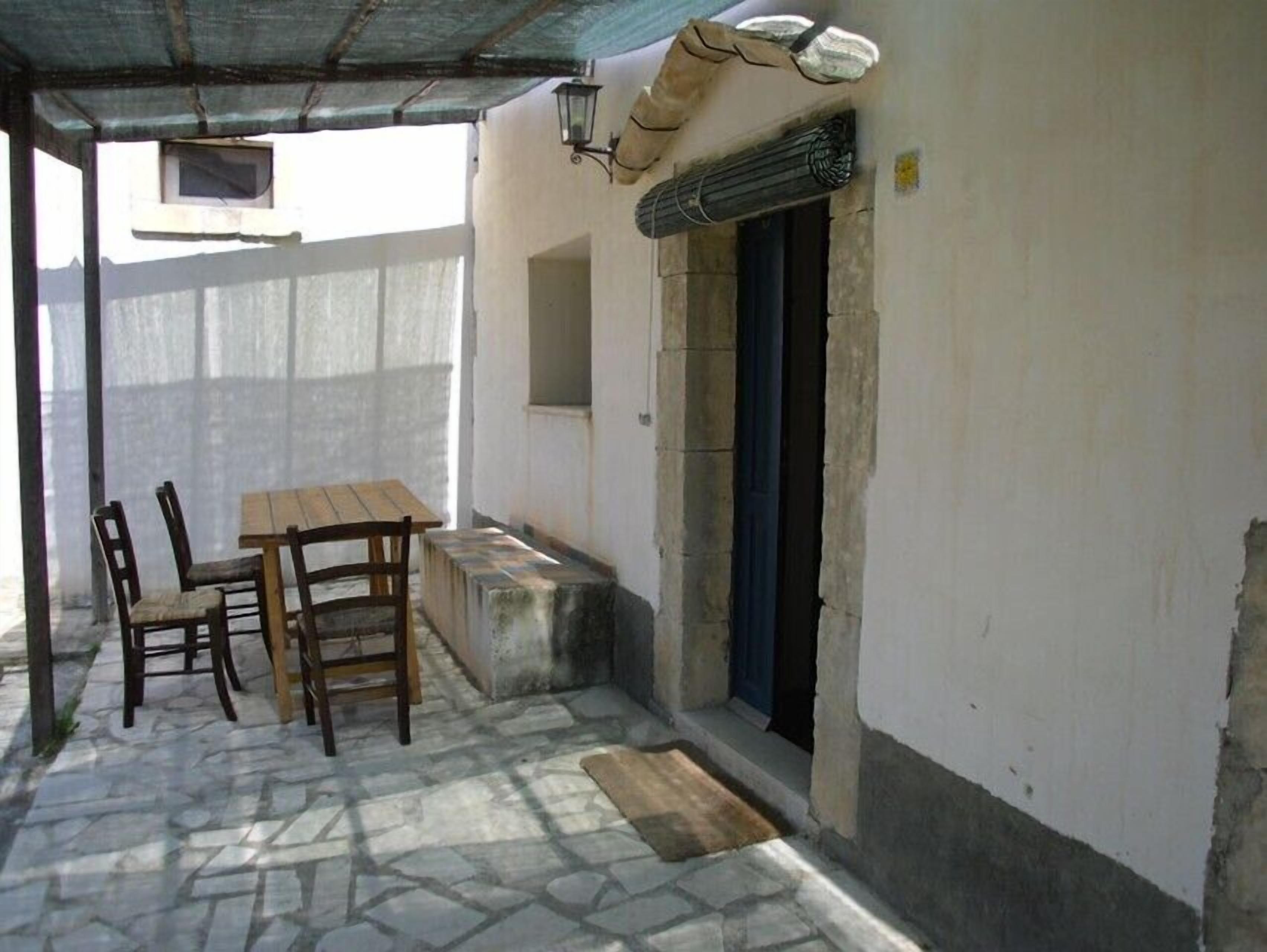 A covered outdoor seating area with a table and chairs, a stone floor, and a door leading to another room.