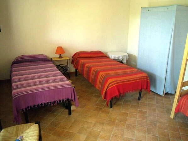 Una habitación con dos camas, una mesita de noche con lámpara y un armario.