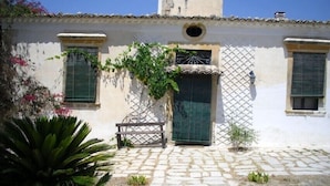 A building with a tiled roof, a central door with a lattice design, and two windows with shutters. - Il Bagolaro (Noto)