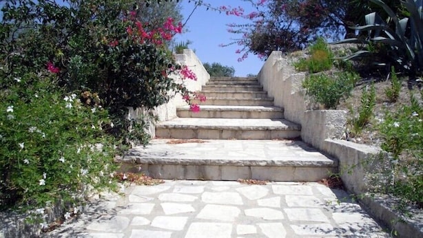 A stone staircase leading up a hill, surrounded by greenery and flowering plants. - Il Bagolaro (Noto)
