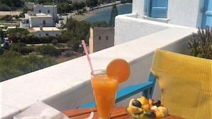 A table with a meal consisting of grilled meats, eggs, and vegetables, a glass of orange juice, and a bowl of fruit. - Hotel Saint George Valsamitis (Amorgos)