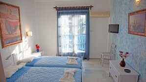 A bedroom with two beds, a nightstand, a dresser, a TV, and a window with curtains. - Hotel Saint George Valsamitis (Amorgos)