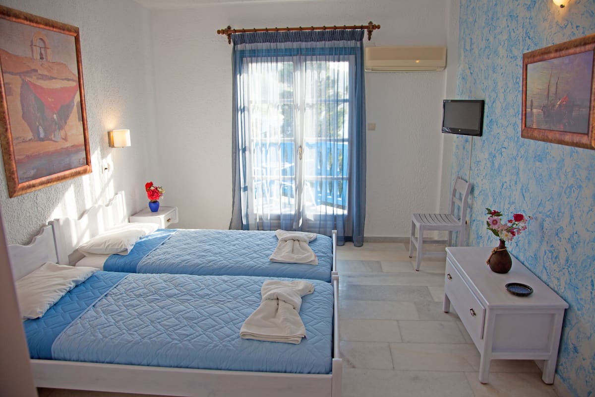 A bedroom with two beds, a nightstand, a dresser, a TV, and a window with curtains.