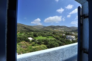 A view from a balcony overlooking a green valley with hills and scattered buildings. - Hotel Saint George Valsamitis (Amorgos)